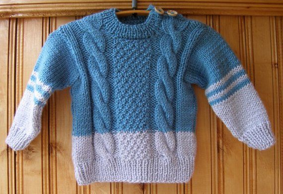Een handgebreide kinderpullover in blauw en lichtgrijs met kabel- en noppenpatronen.